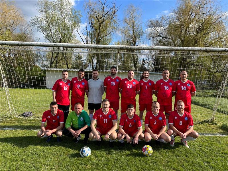 Soccer team posing for a photo on a grass field with a goalpost in the background.